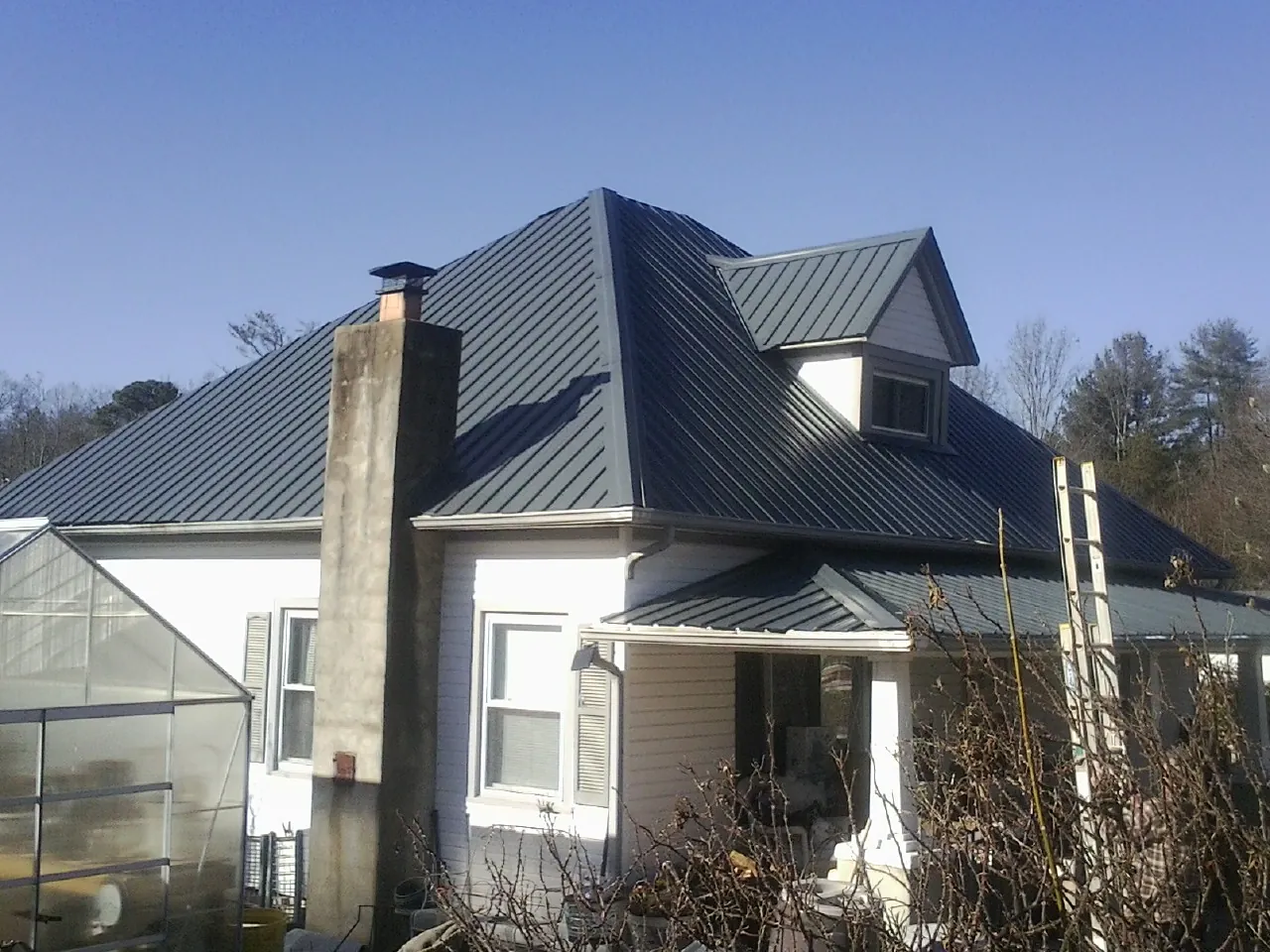 Dark blue standing seam metal roof on a white farmhouse with dormer — Slate & Tile Roof Repair by Roofing Brothers in Remsenburg