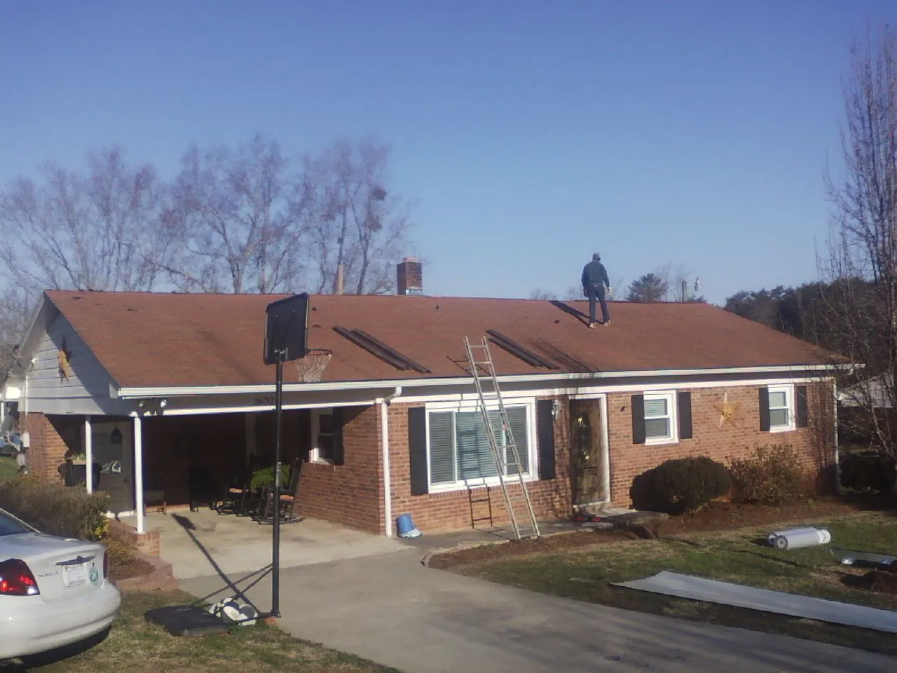 Roofer stripping a shingle roof on a brick ranch before metal panels in Remsenburg