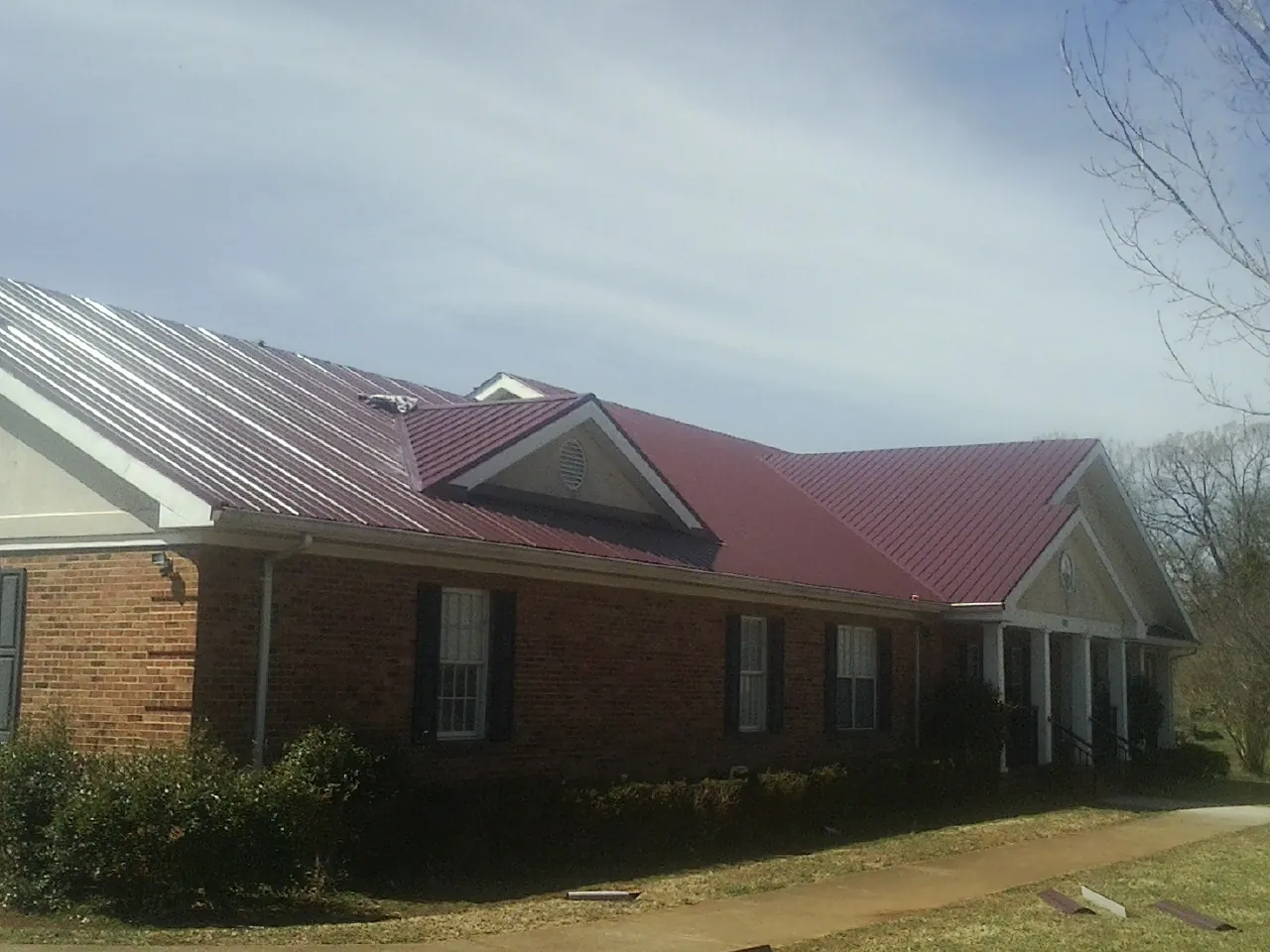 Red metal roof with gabled entries on a long brick building, from a Hail Damage Roof Repair job in Remsenburg