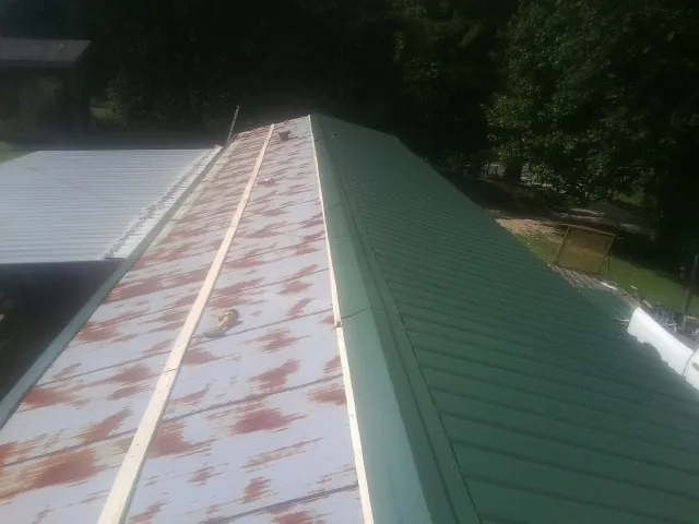 Old rusted panels beside newly installed green metal roofing — Wind Damage Roof Repair by Roofing Brothers in Remsenburg