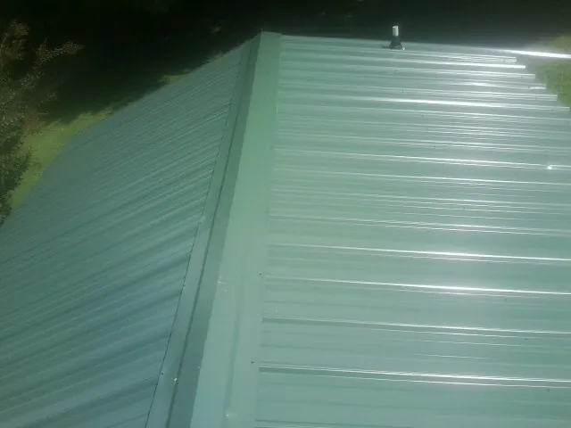 New green metal panels meeting at the ridge of a roof — Flat Roof Repair work by our crew in Remsenburg
