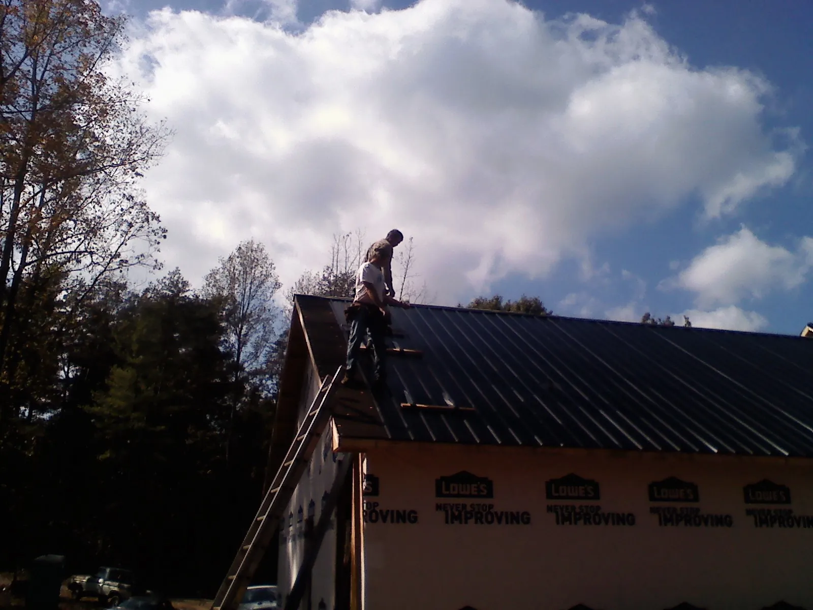 Roofer fastening dark metal panels high against a cloudy sky, from a Roof Inspection job in Remsenburg