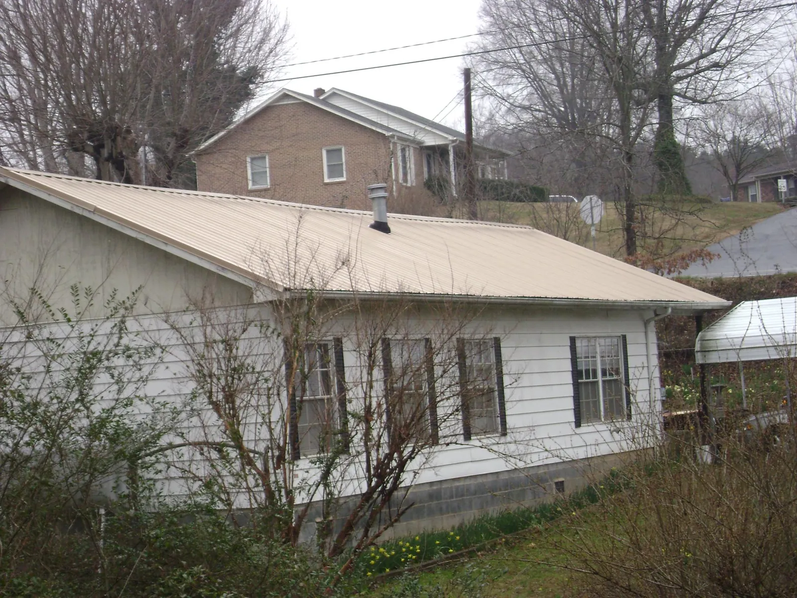 Tan metal roof on a white sided house set into a hillside — Commercial Roofing by Roofing Brothers in Remsenburg